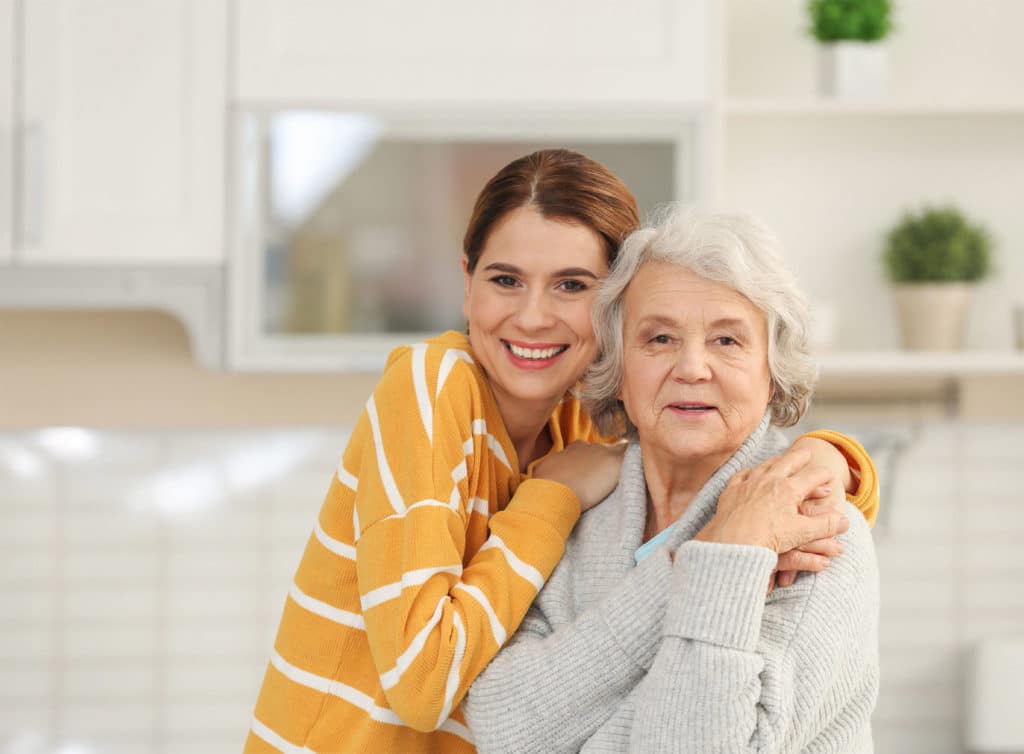 A young female caretaker and a senior woman smiling at the camera