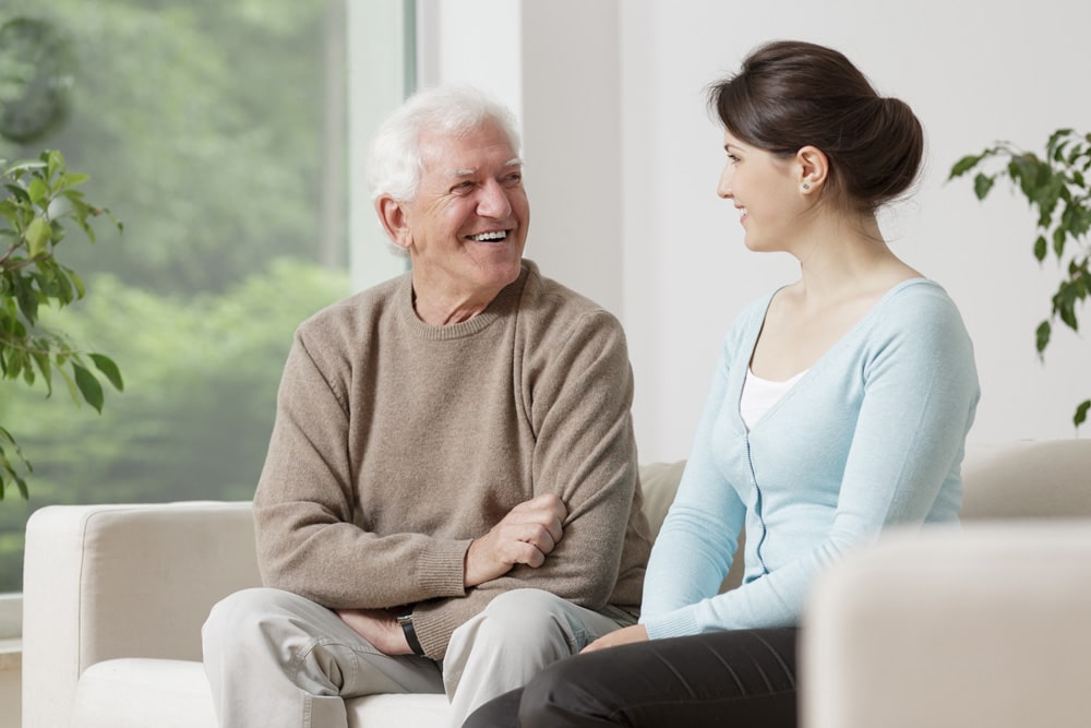 A senior man and a young female caretaker having a conversation on a couch