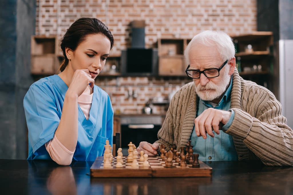 female caregiver playing chess with senior male